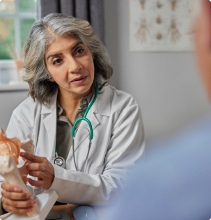 Mature Female Doctor Meeting With Male Patient Discussing Joint Pain In Hip Using Anatomical Model